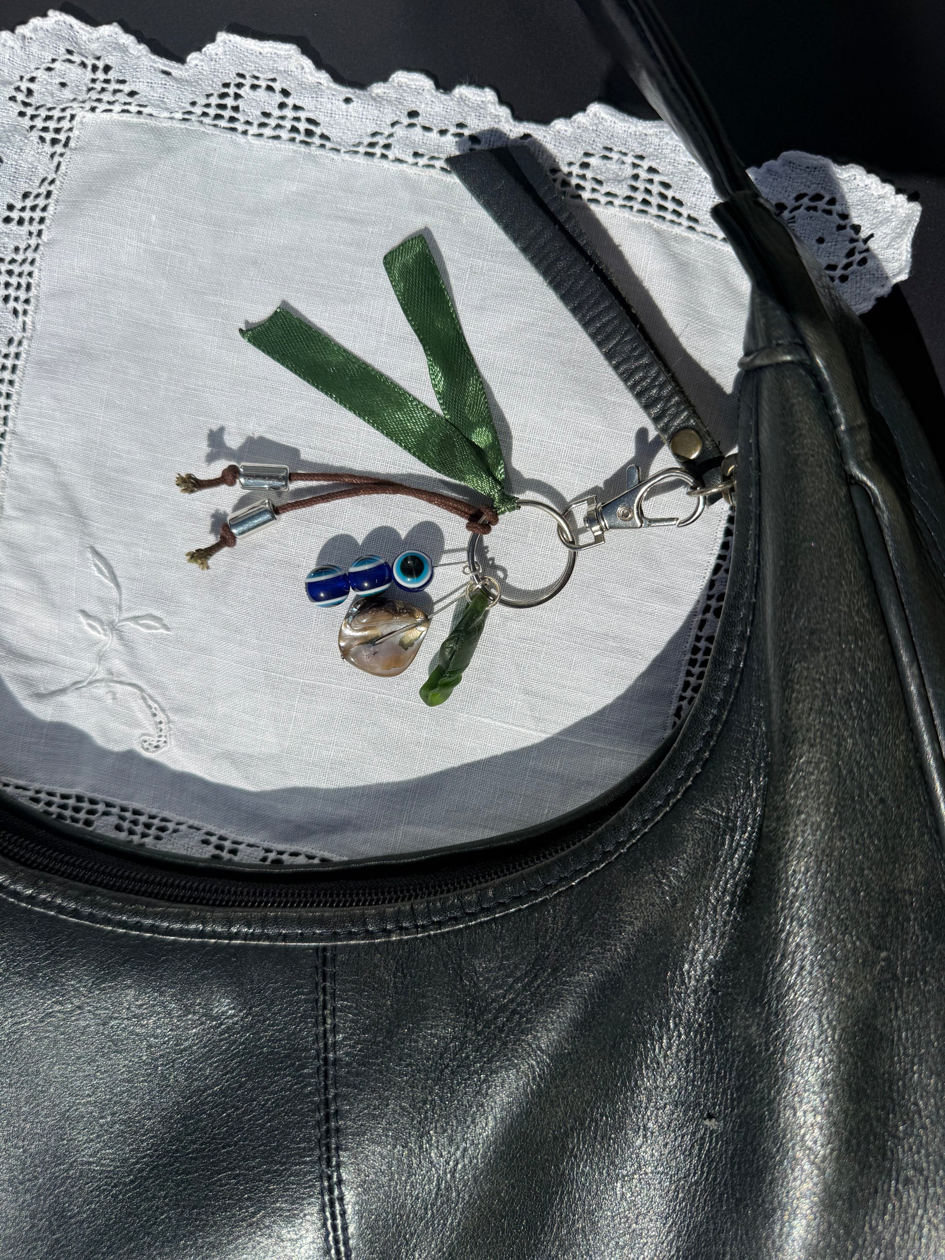 Keychain with a small bird design attached to a black leather bag on a white doily.