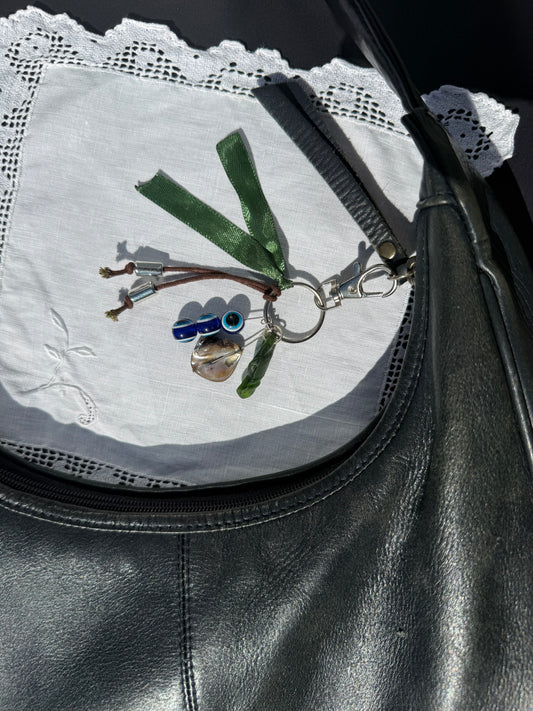 Keychain with a small bird design attached to a black leather bag on a white doily.