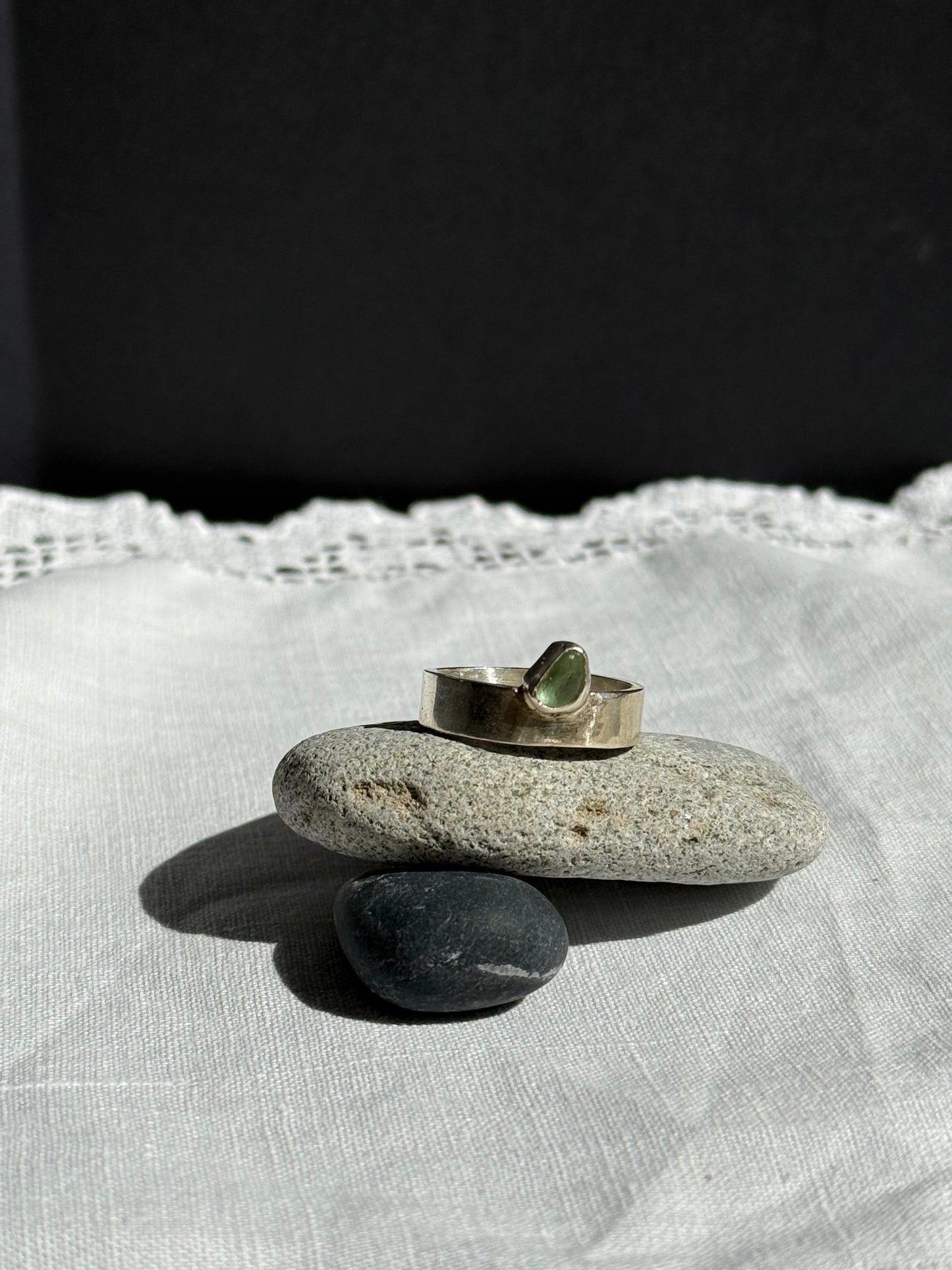 Silver ring with a green stone on a pebble over a white fabric background