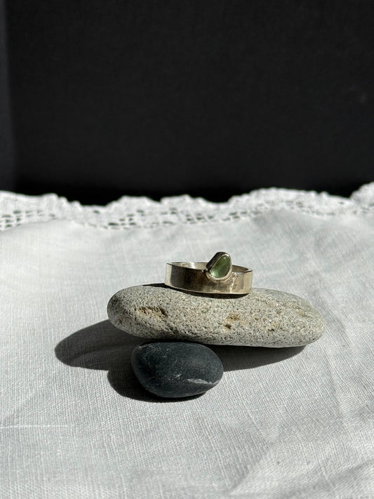 Silver ring with a green stone on a pebble over a white fabric background