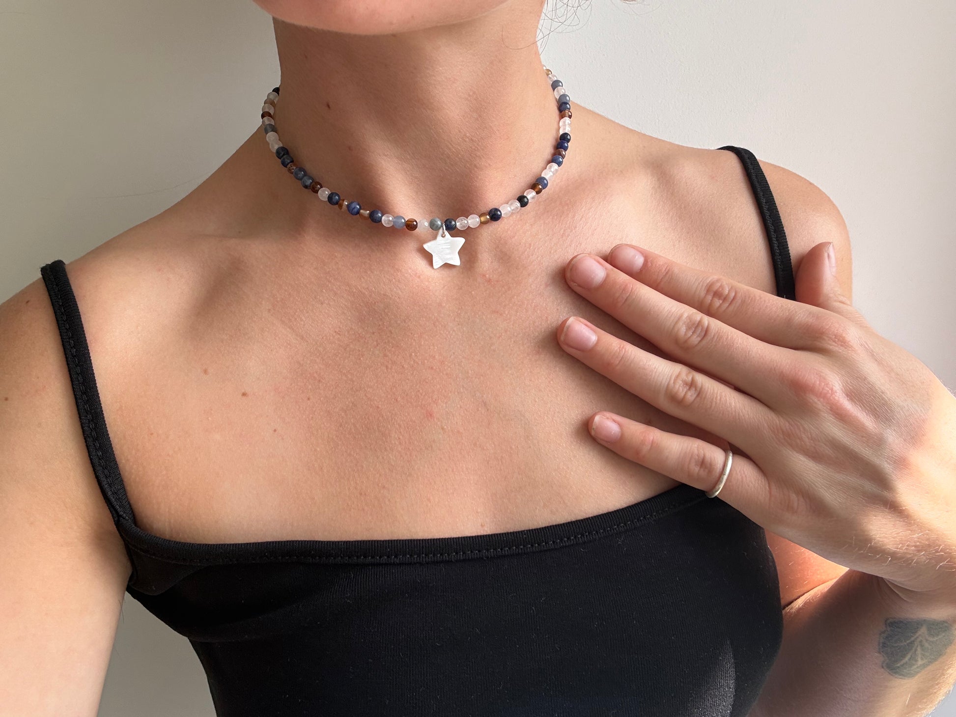 Person wearing a beaded necklace with a star pendant, hand touching chest.