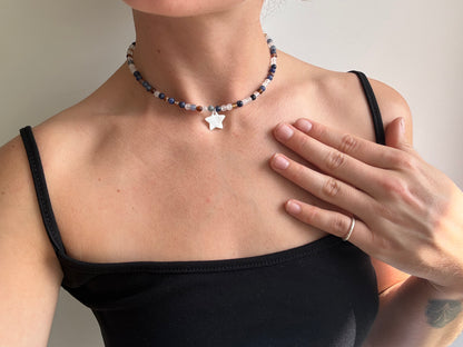 Person wearing a beaded necklace with a star pendant, hand touching chest.